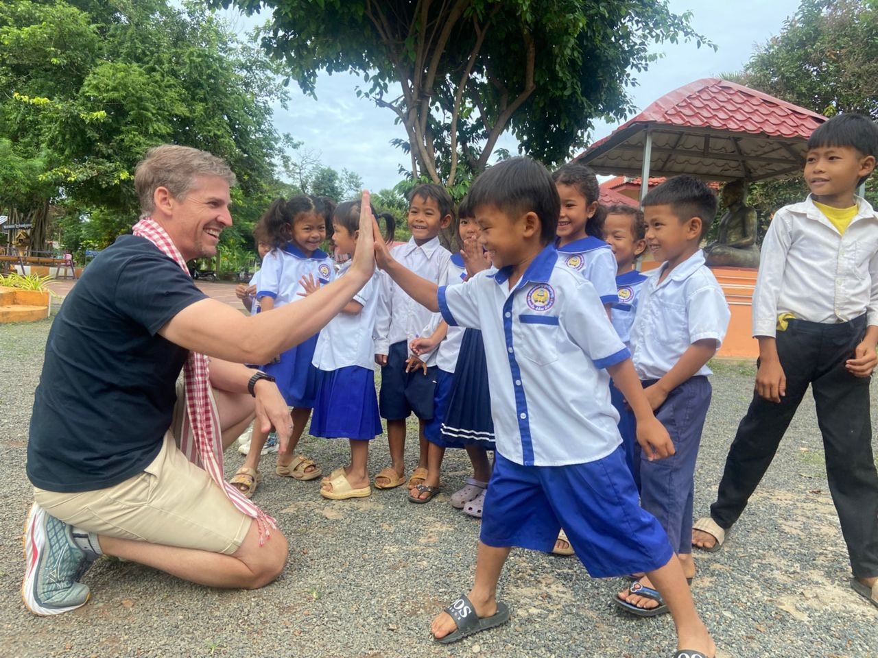 James Grafas high-fiving a student outside one of the schools in Baribour District, Kampong Chhnang — January 2026 project visit