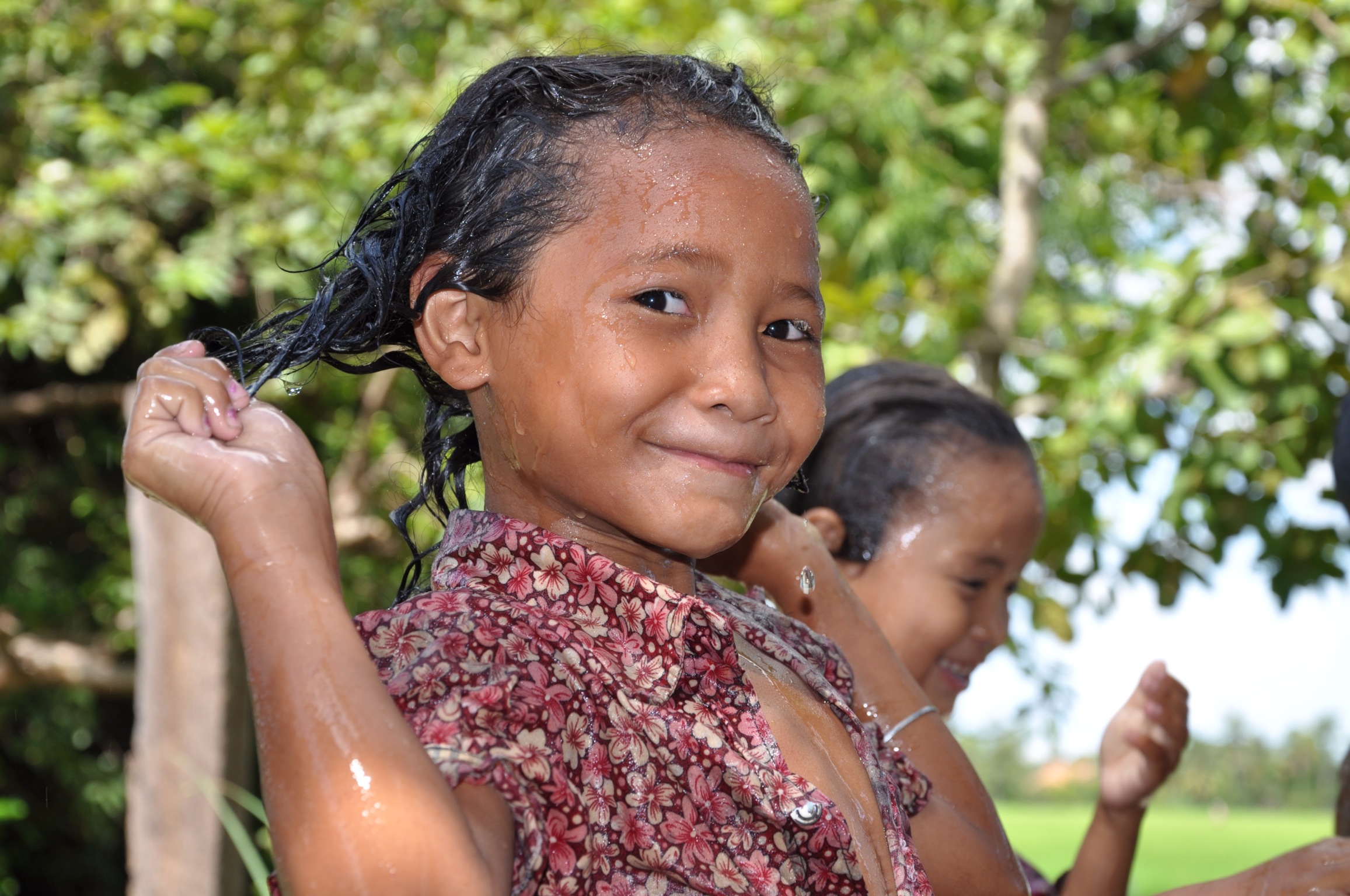 A girl with wet hair smiling after washing at a new school water point