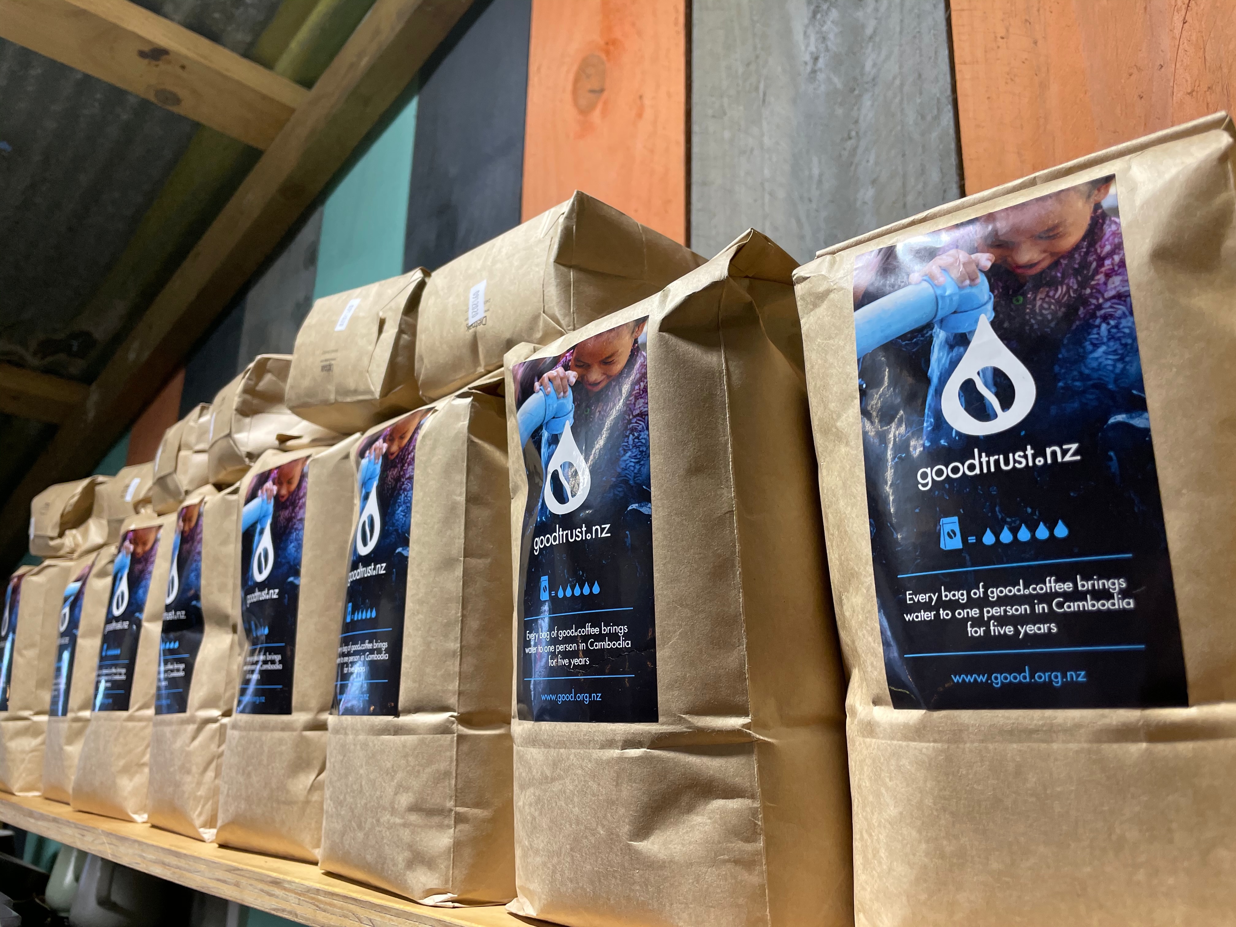 A shelf of good.coffee bags branded goodtrust.nz — every bag funds clean water in Cambodia for one person for five years