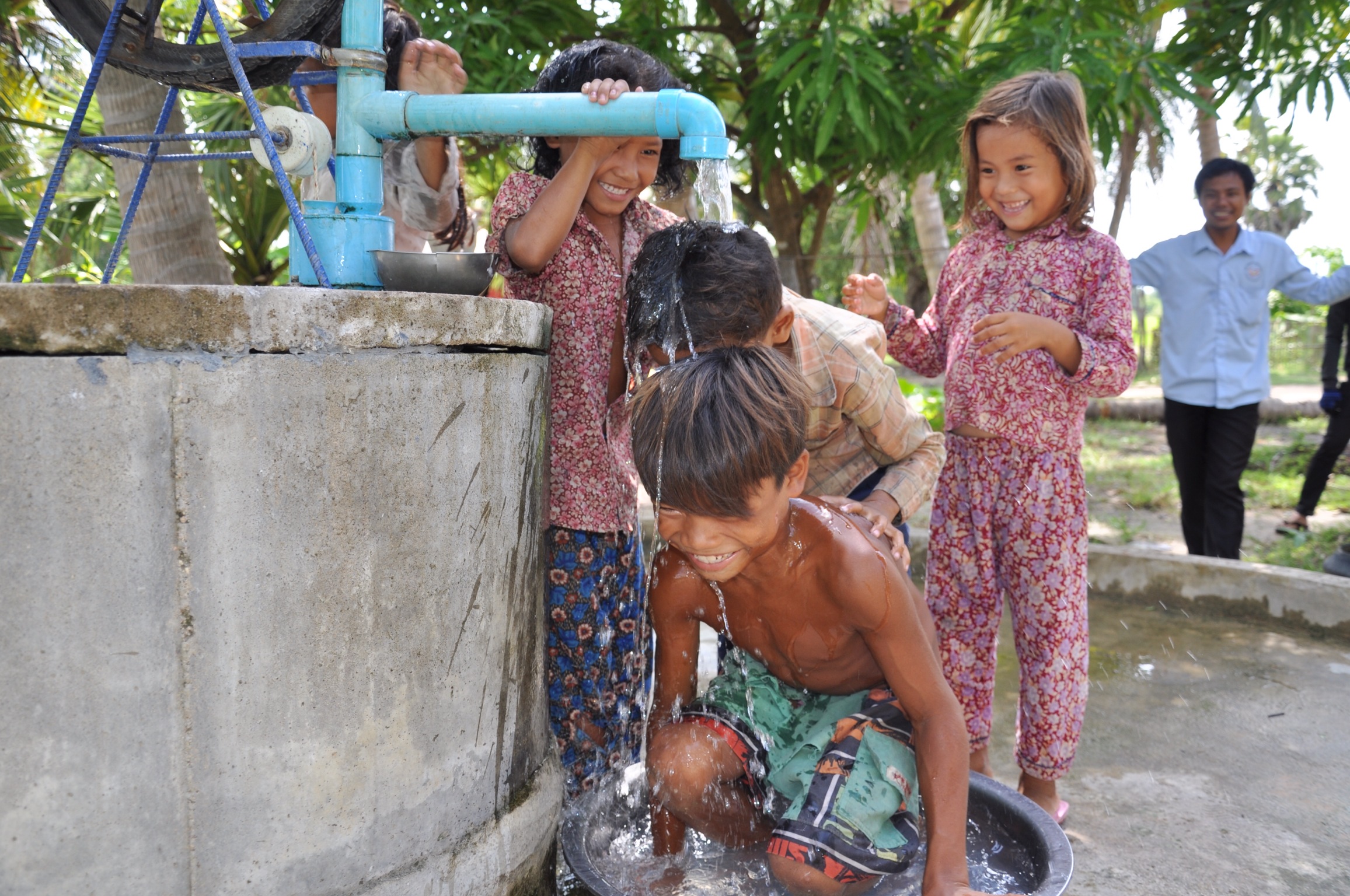 Children laughing and splashing under the spout of a newly completed Good Trust well in rural Cambodia