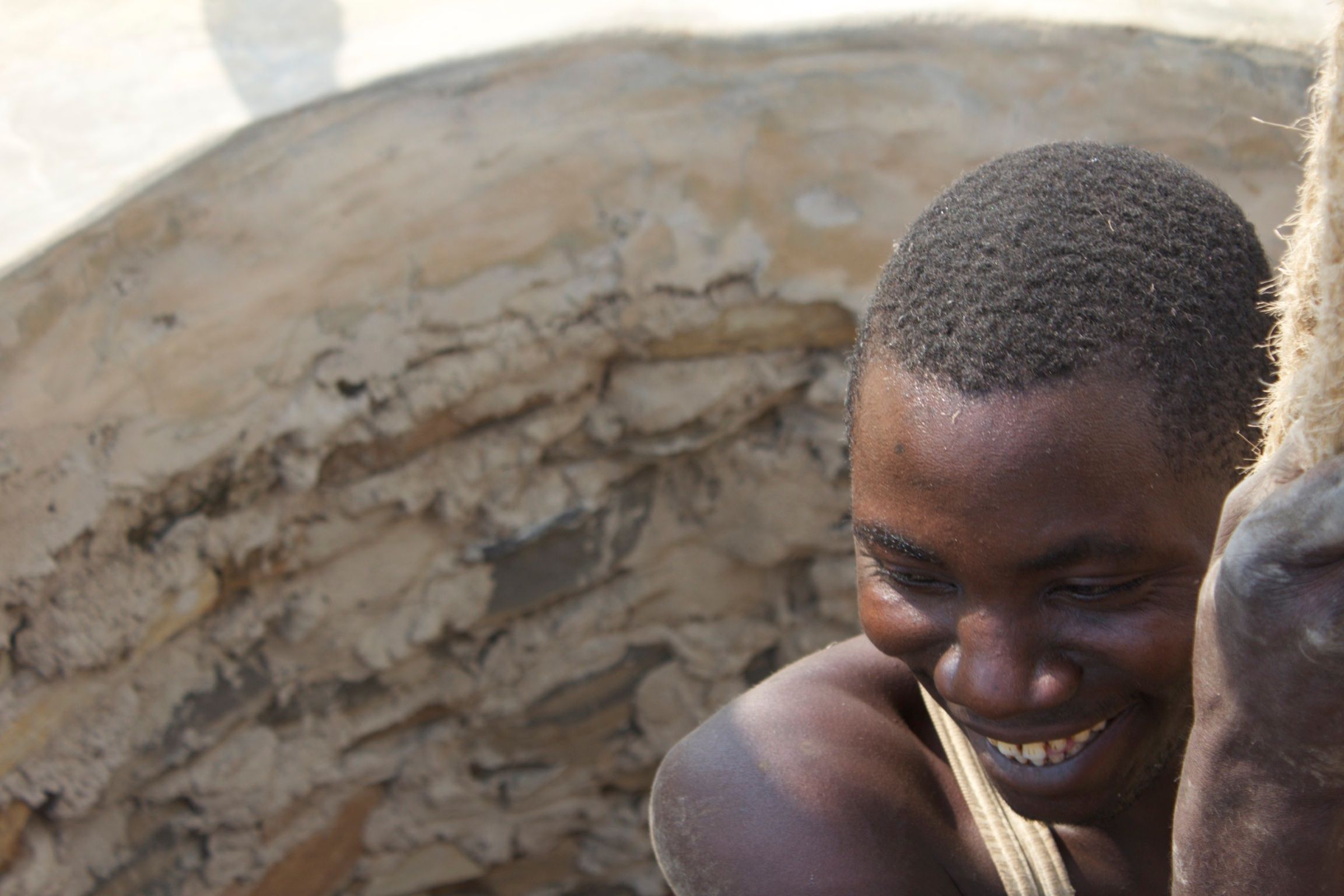 A young man emerging from a hand-dug well shaft, smiling at the camera — one of Good Trust's earliest projects in Cambodia, 2011